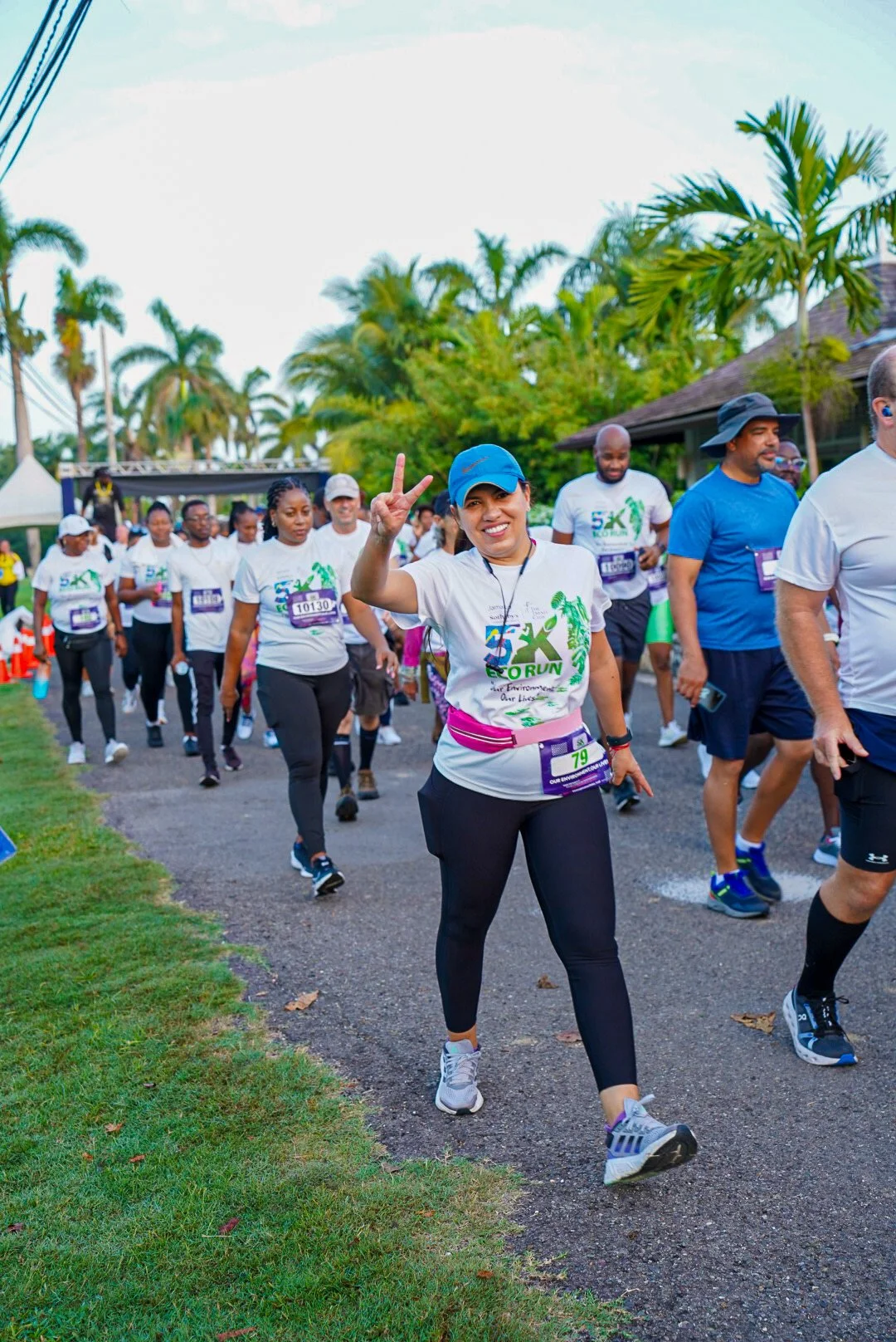 Group of people participating in a 5K run or walk event, wearing race bibs and athletic clothing, walking along a path lined with palm trees.