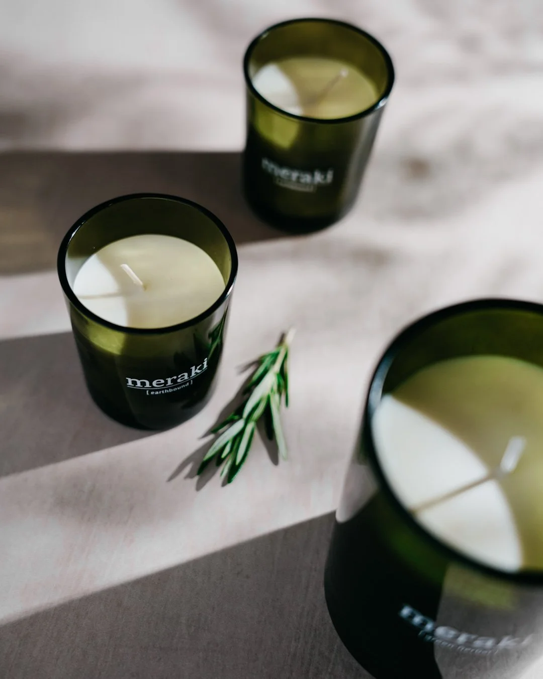 Three black candles labeled "meraki" on a wooden surface with a sprig of rosemary