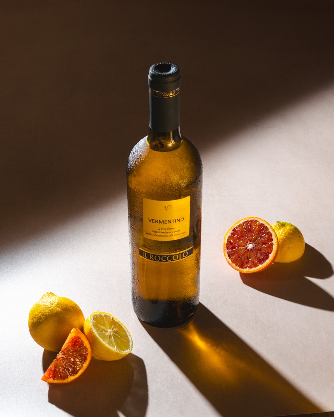 Bottle of Vermentino wine with sliced lemons and blood oranges on a table.