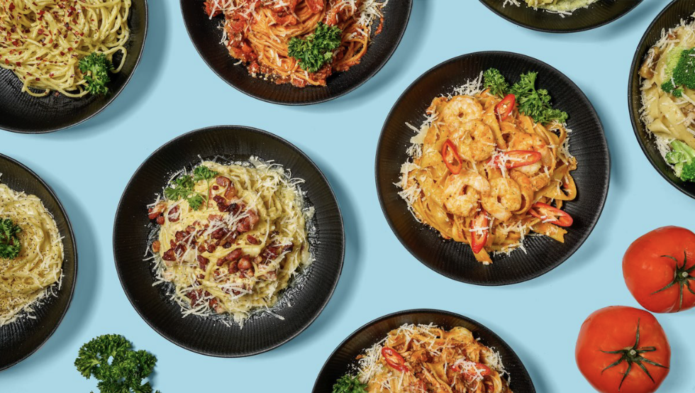 Various bowls of pasta with different sauces and toppings, three tomatoes, and some parsley on a light blue background.