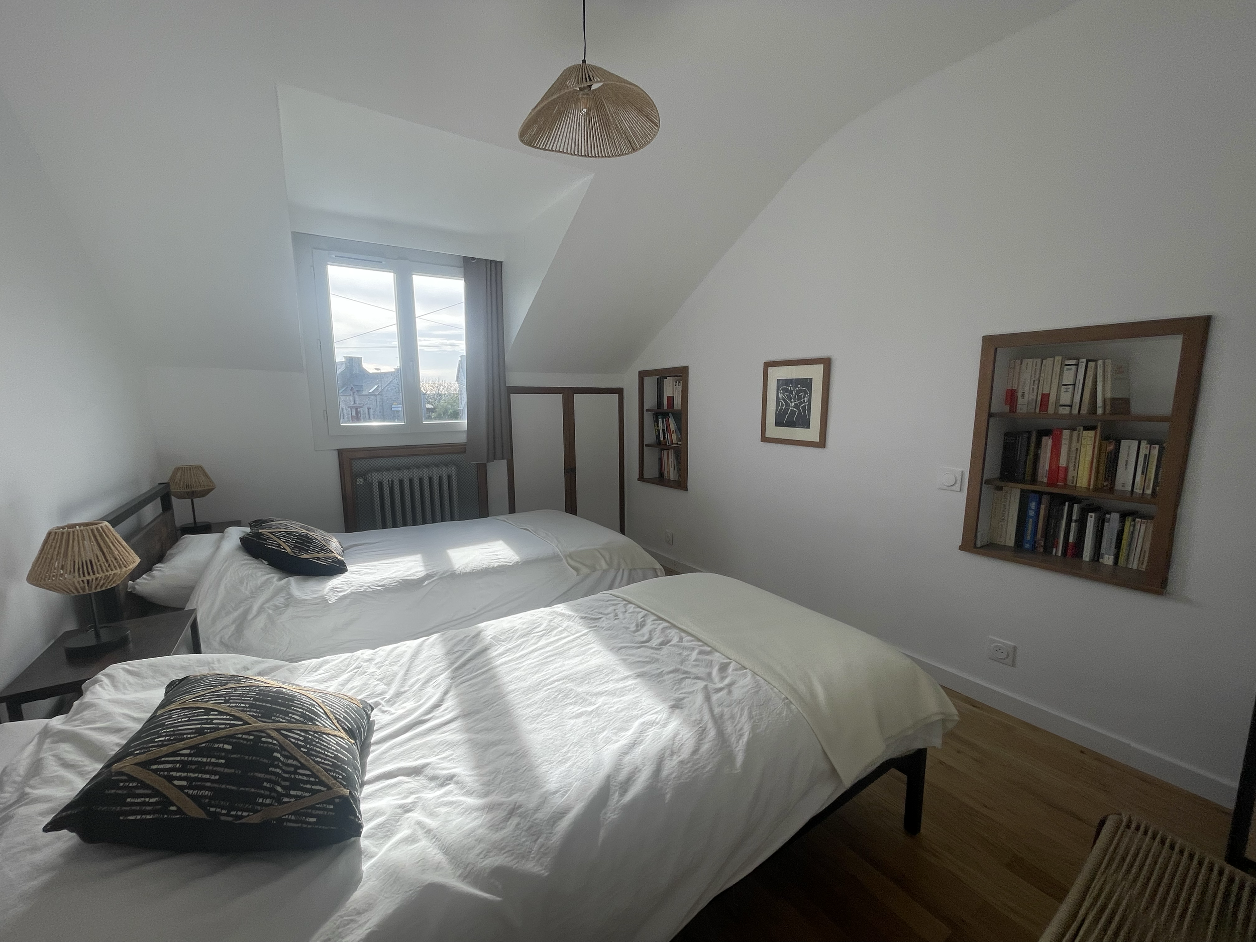 Chambre avec deux lits, deux lampes en rotin, un cadre photo, une fenêtre avec vue sur le ciel.