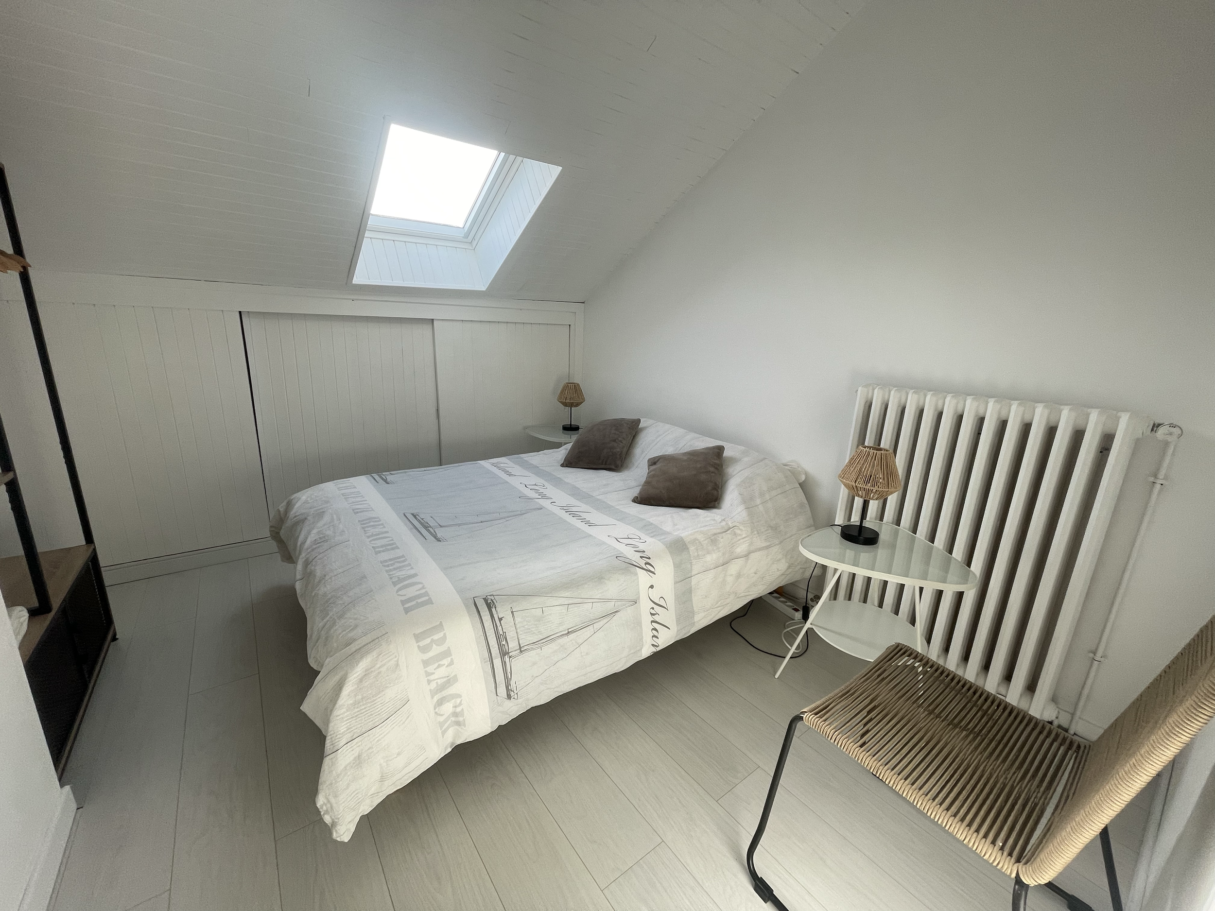 Une chambre avec un lit, deux lampes et un plafonnier dans un toit en pente avec une verrière naturelle.