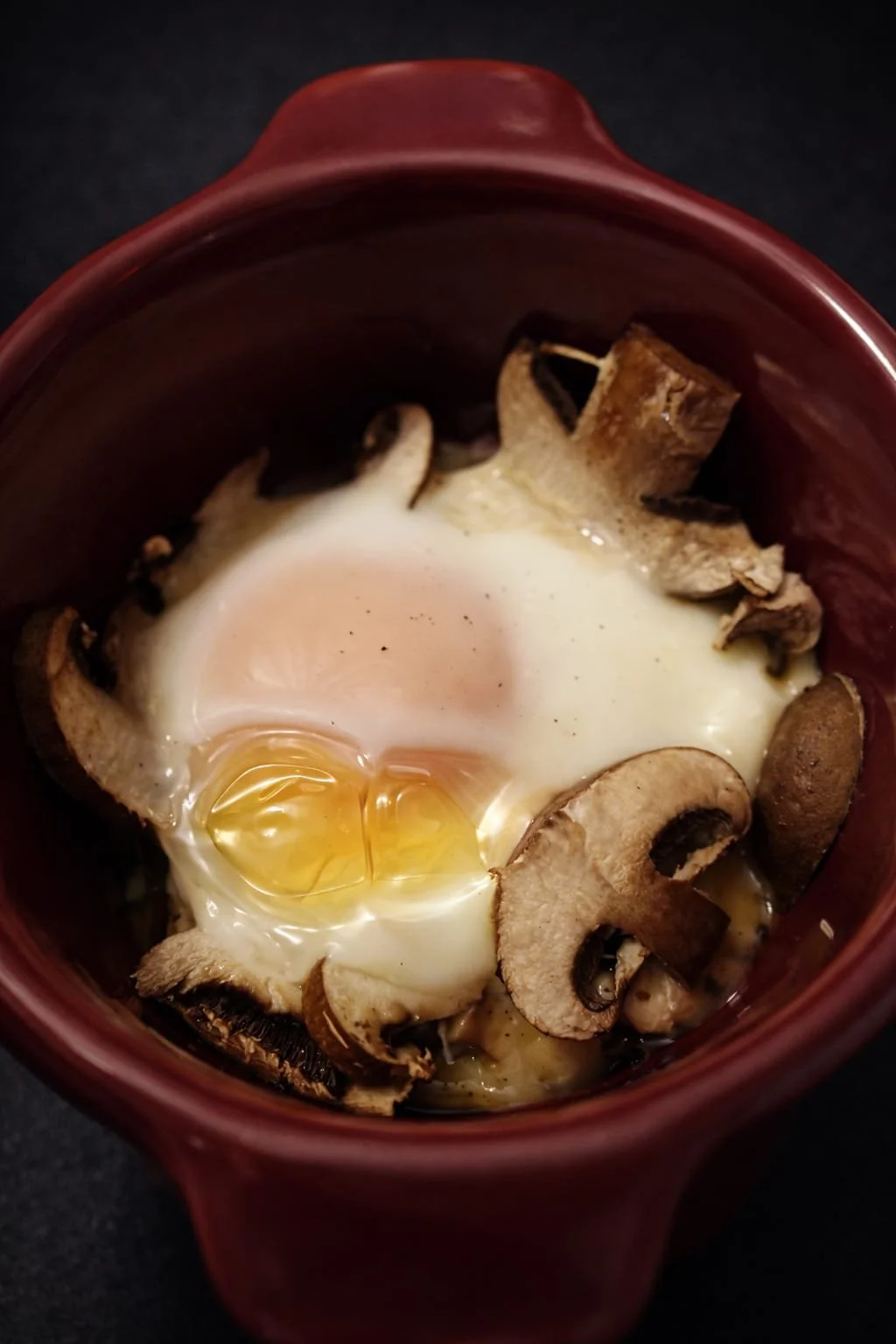 Œuf au plat dans un ramequin rouge avec des champignons tranchés.
