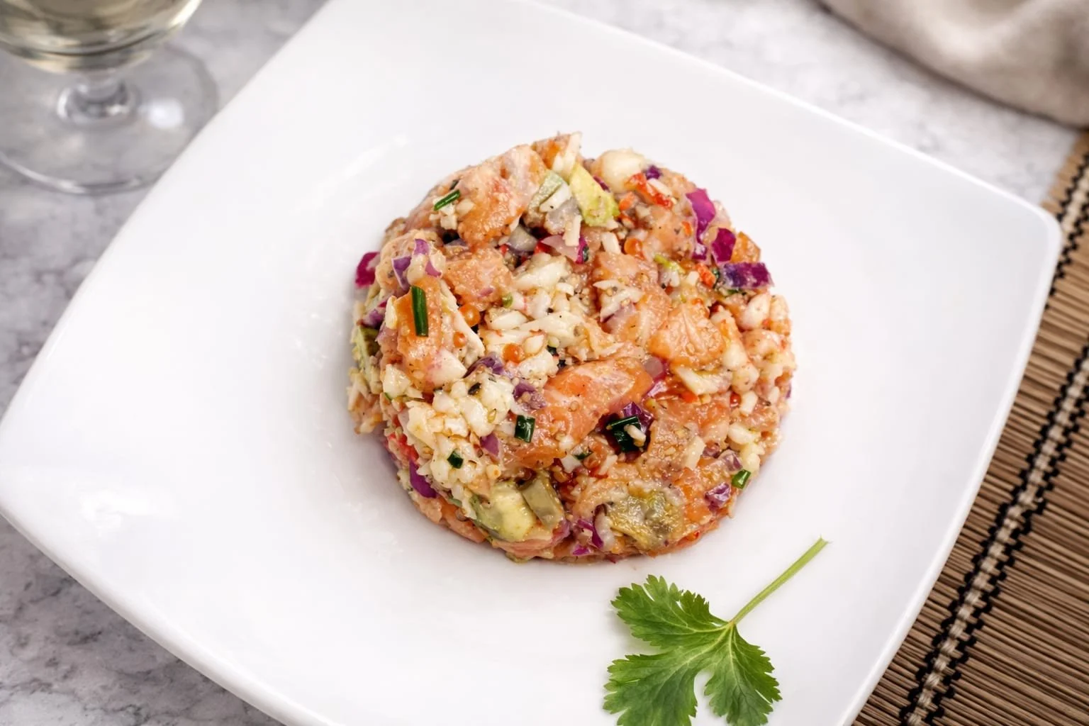 Salade de fruits de mer avec saumon, avocat, oignons rouges et herbes, servie sur une assiette blanche garnie d'une feuille de coriandre.
