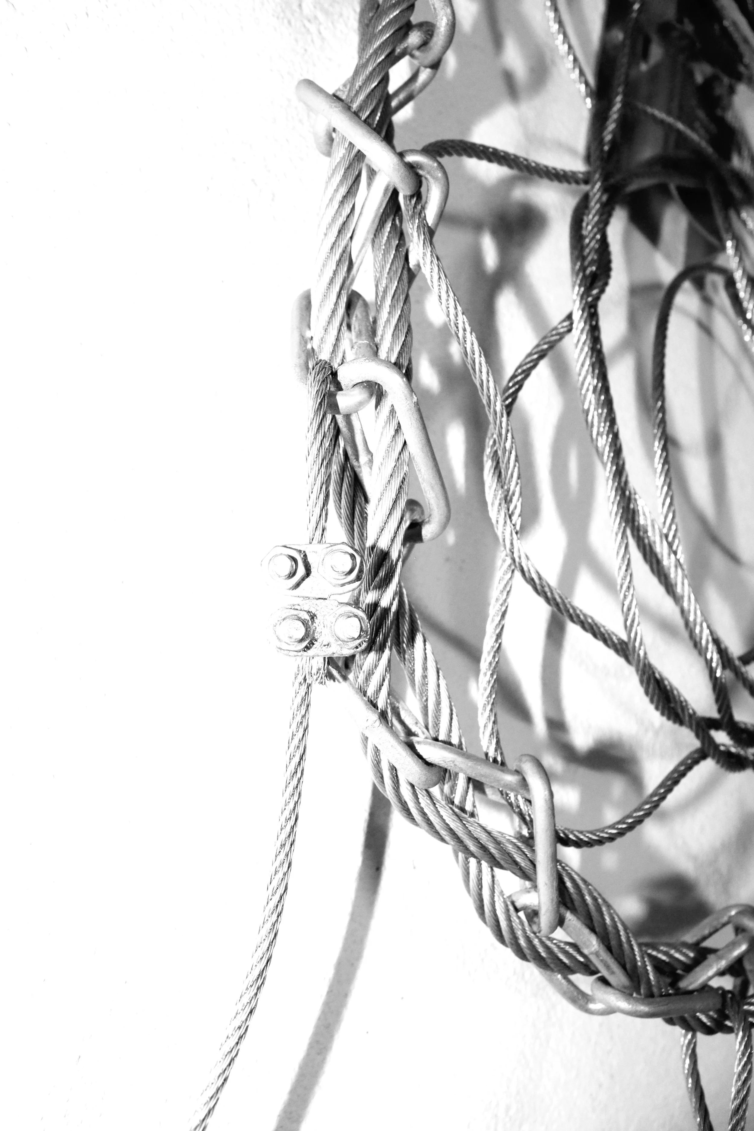 Black and white photo of tangled metal wires and hooks on a white wall. Asibkaashi Metal Dreamcatcher Daniel Alexander Weiter - DAW
