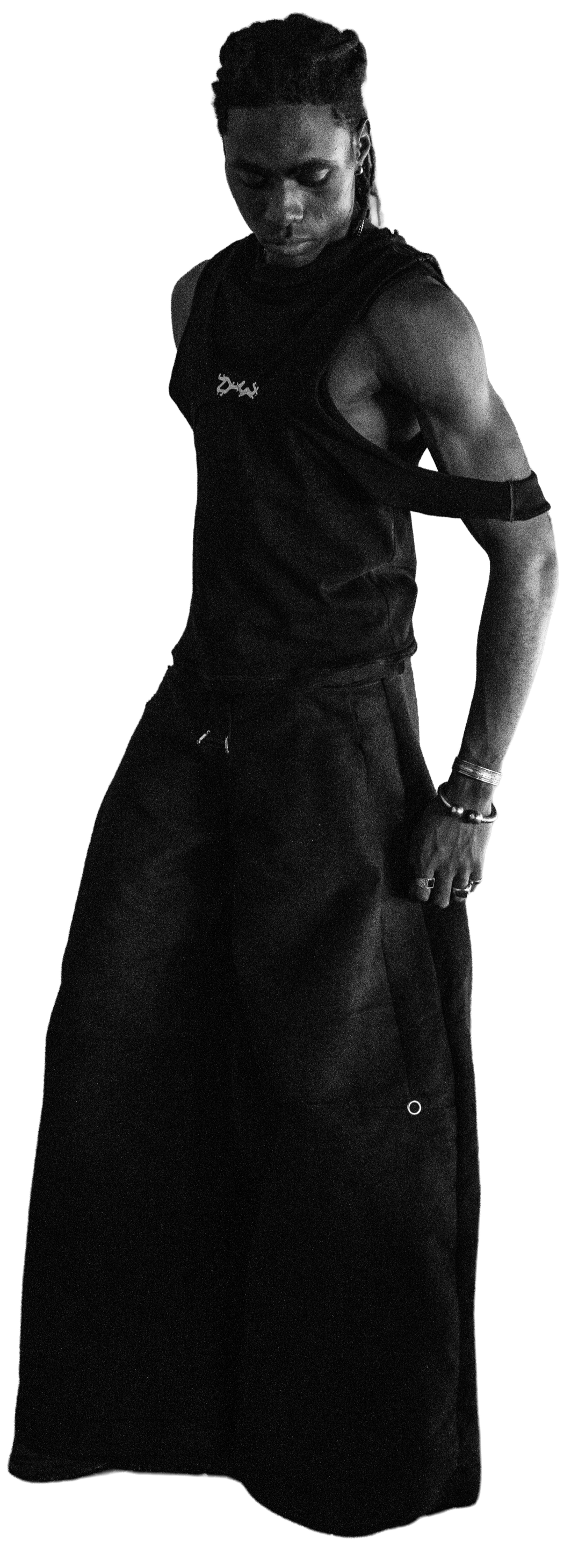 A Black man in dark clothing stands with his head bowed and eyes closed, wearing a Twisted tank top and wide-leg pants, against a plain background. Daniel Alexander Weiter - DAW