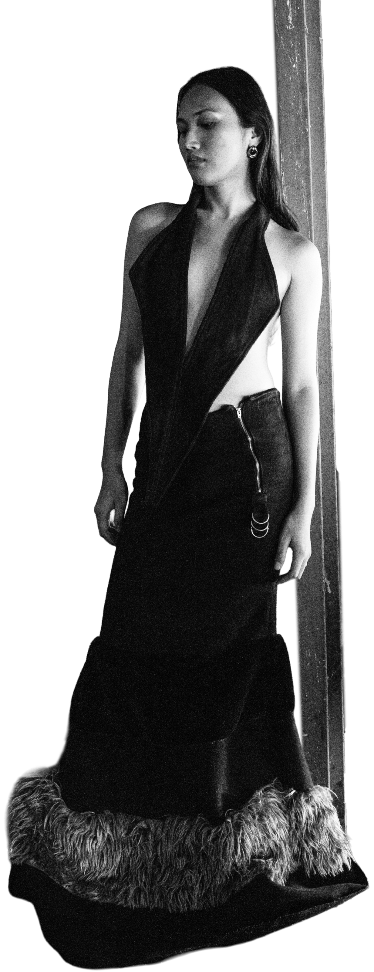 A woman wearing a black dress with a deep V neckline and open sides, standing against a plain background. The dress features a zipper detail on the skirt with fur trim at the bottom. Daniel Alexander Weiter - DAW