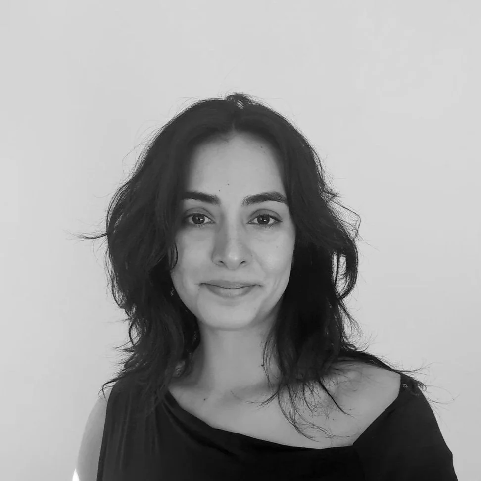 Black and white portrait of a young woman with wavy dark hair, wearing a black top, smiling subtly, against a plain background.