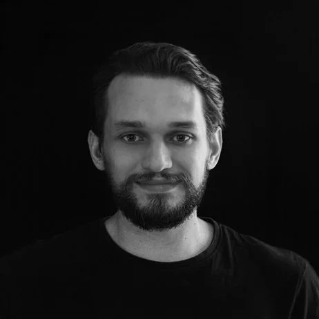 Portrait of a man with a beard and mustache, smiling slightly, against a black background.