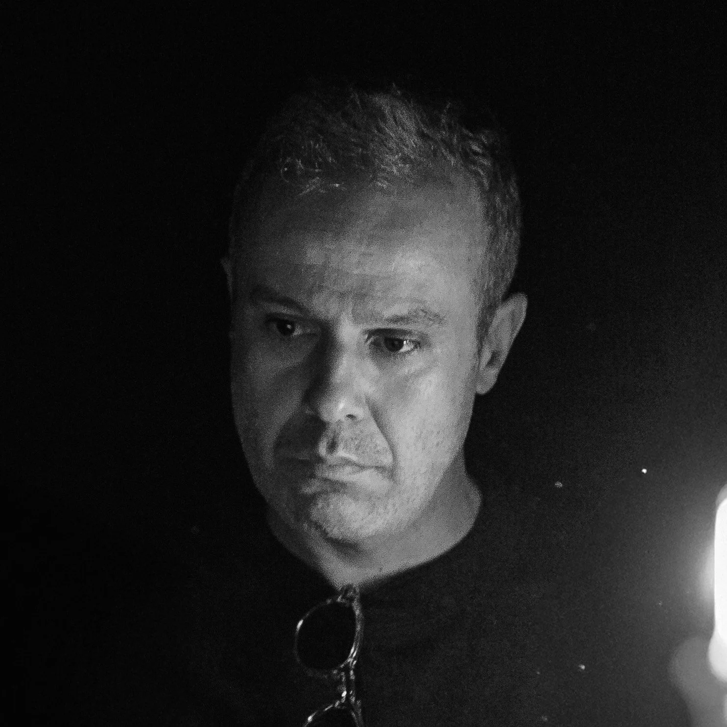 Black and white photo of a man looking at a lit candle in darkness.