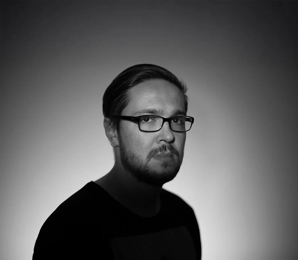 Black and white portrait of a man with glasses, mustache, and beard, looking at the camera with a serious expression.