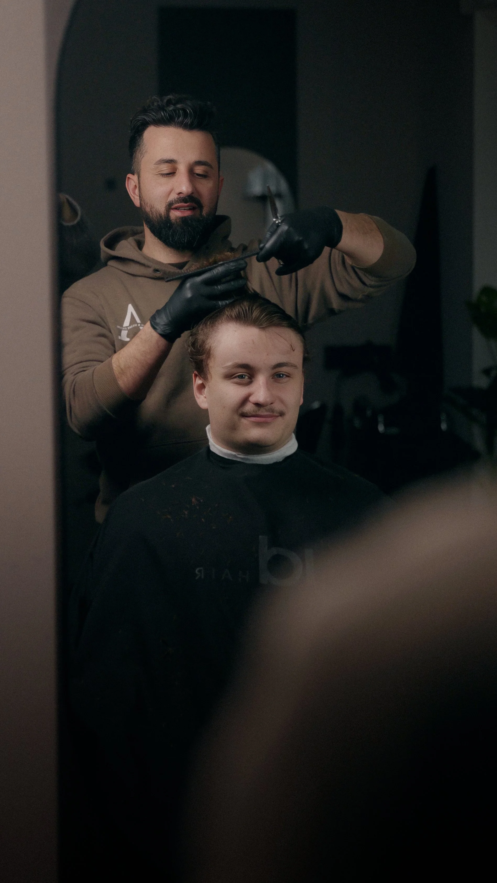 En barber, der klipper en mands hår, set gennem spejl.