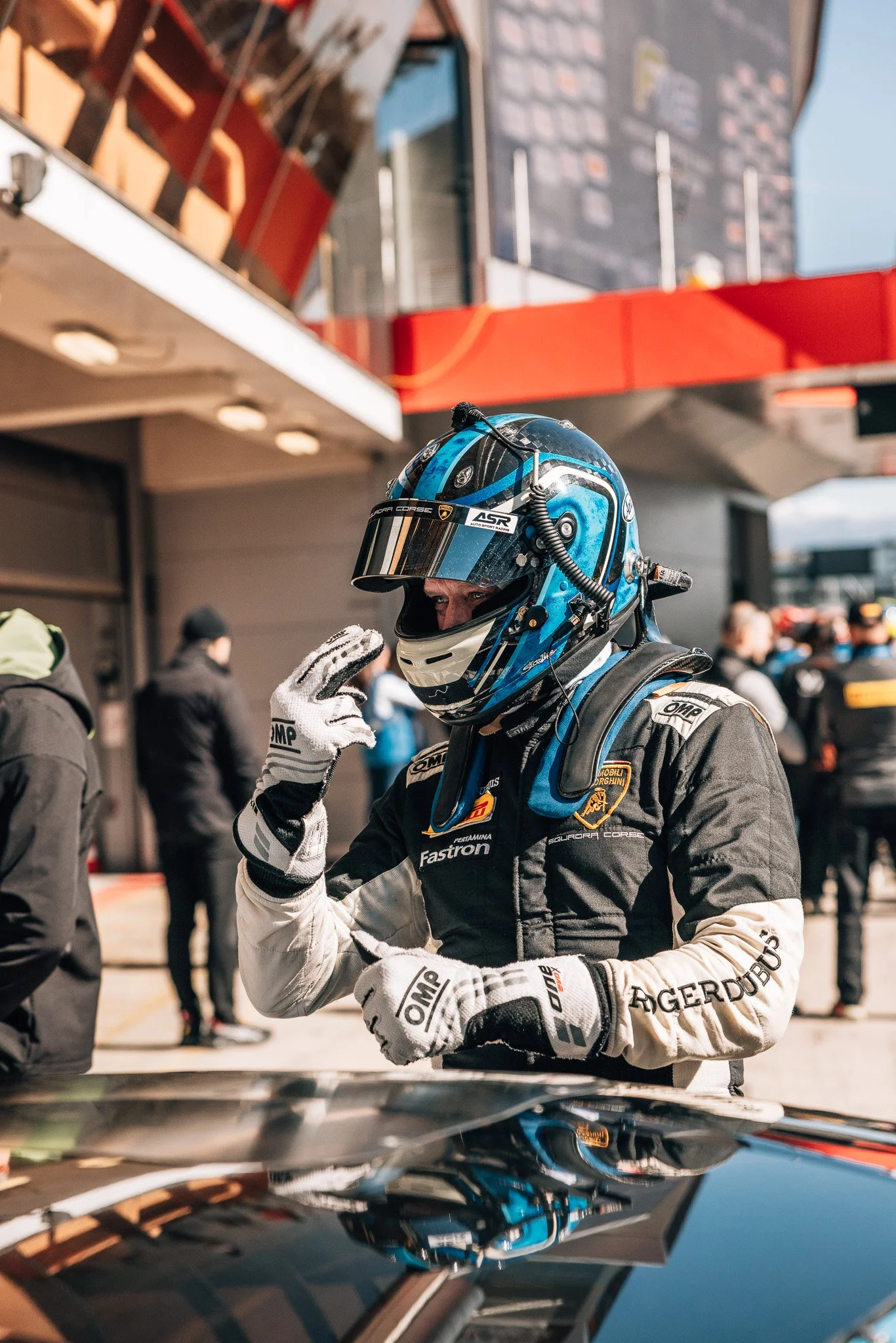 Race car driver in racing suit and helmet adjusting his gloves in the pit lane