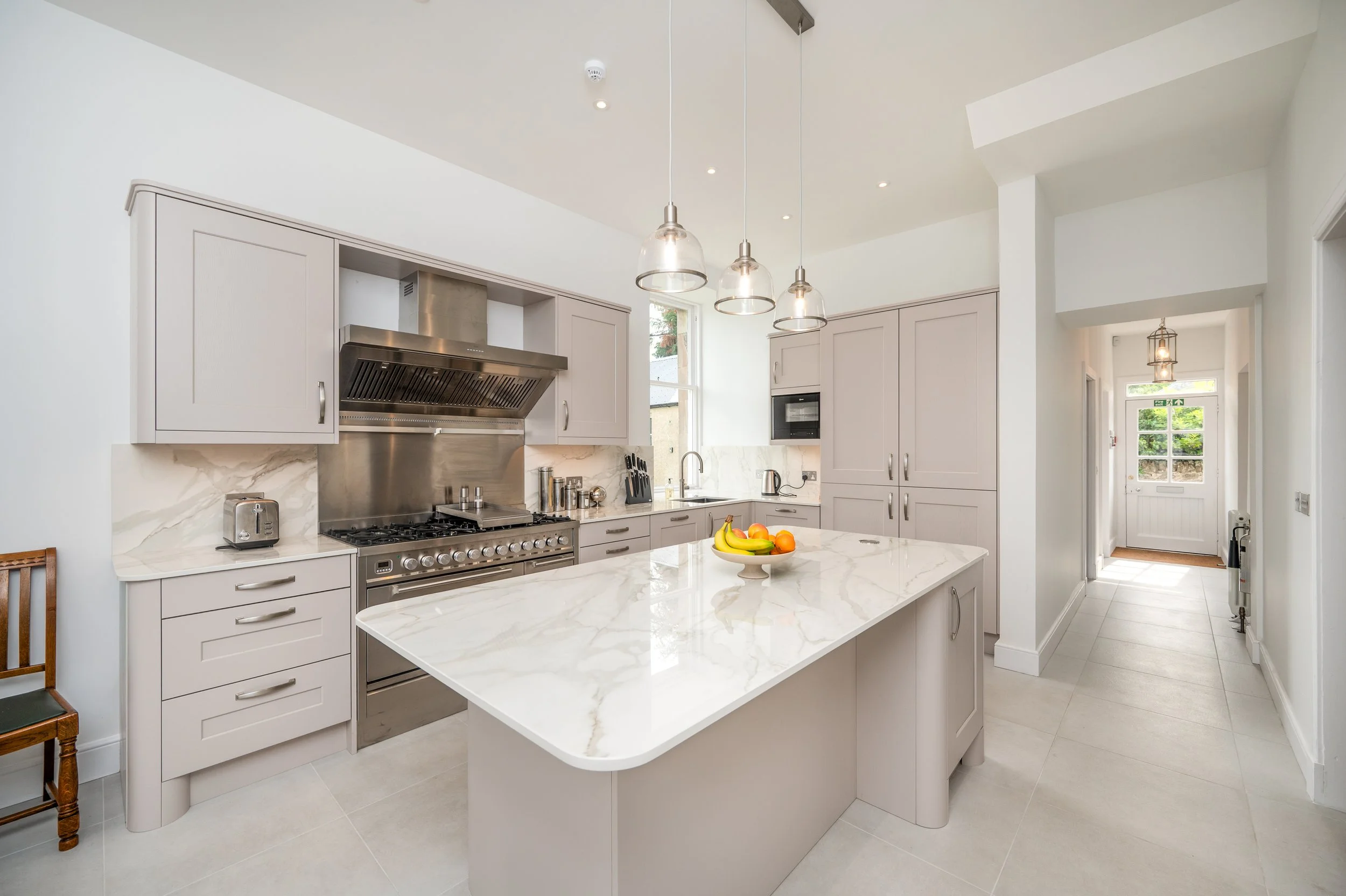 Modern kitchen with light gray cabinets, black glass appliances, and plaid window blinds.