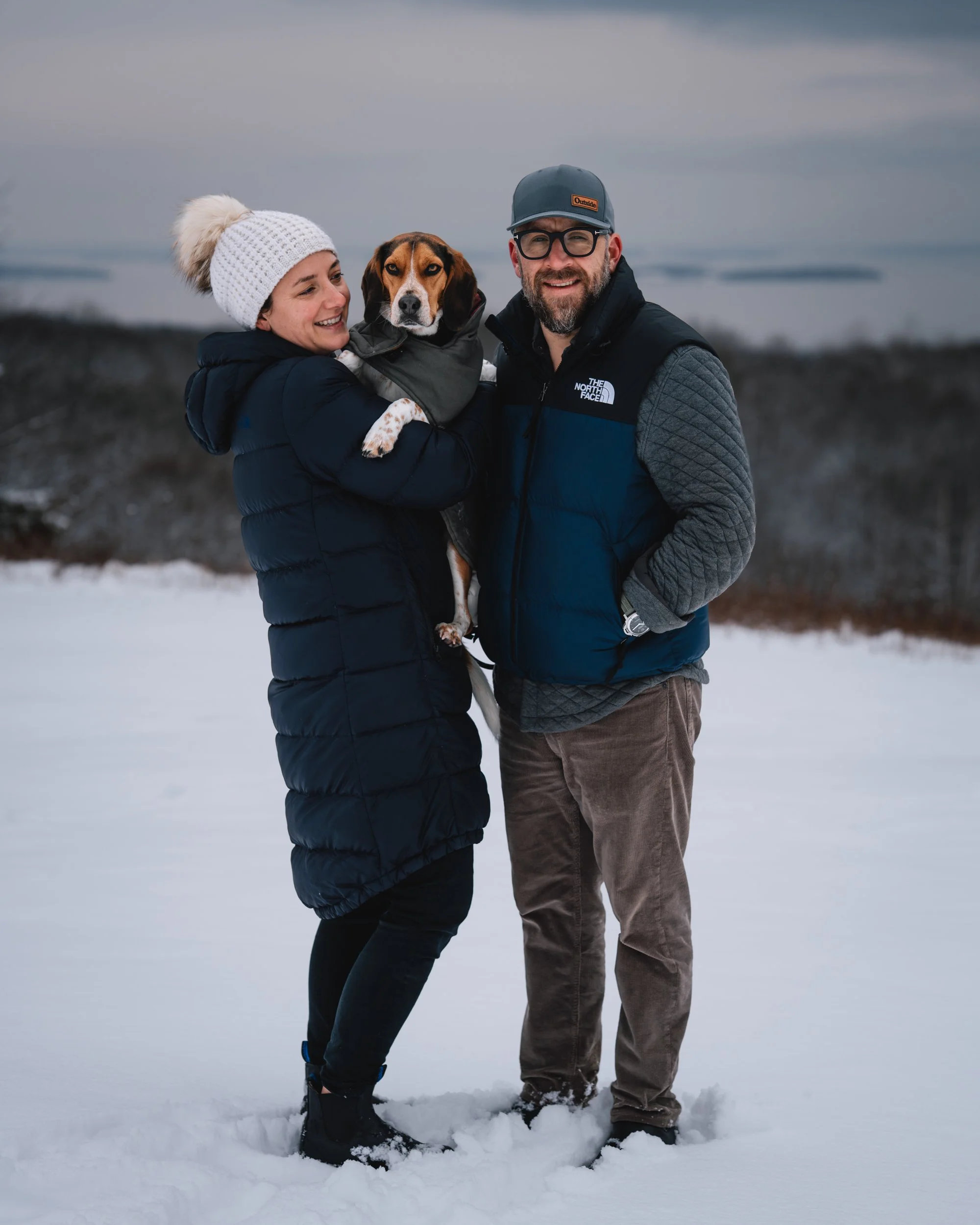 Couple holding their beagle during a winter pet photography session at Beech Hill Preserve in Rockport, Maine.