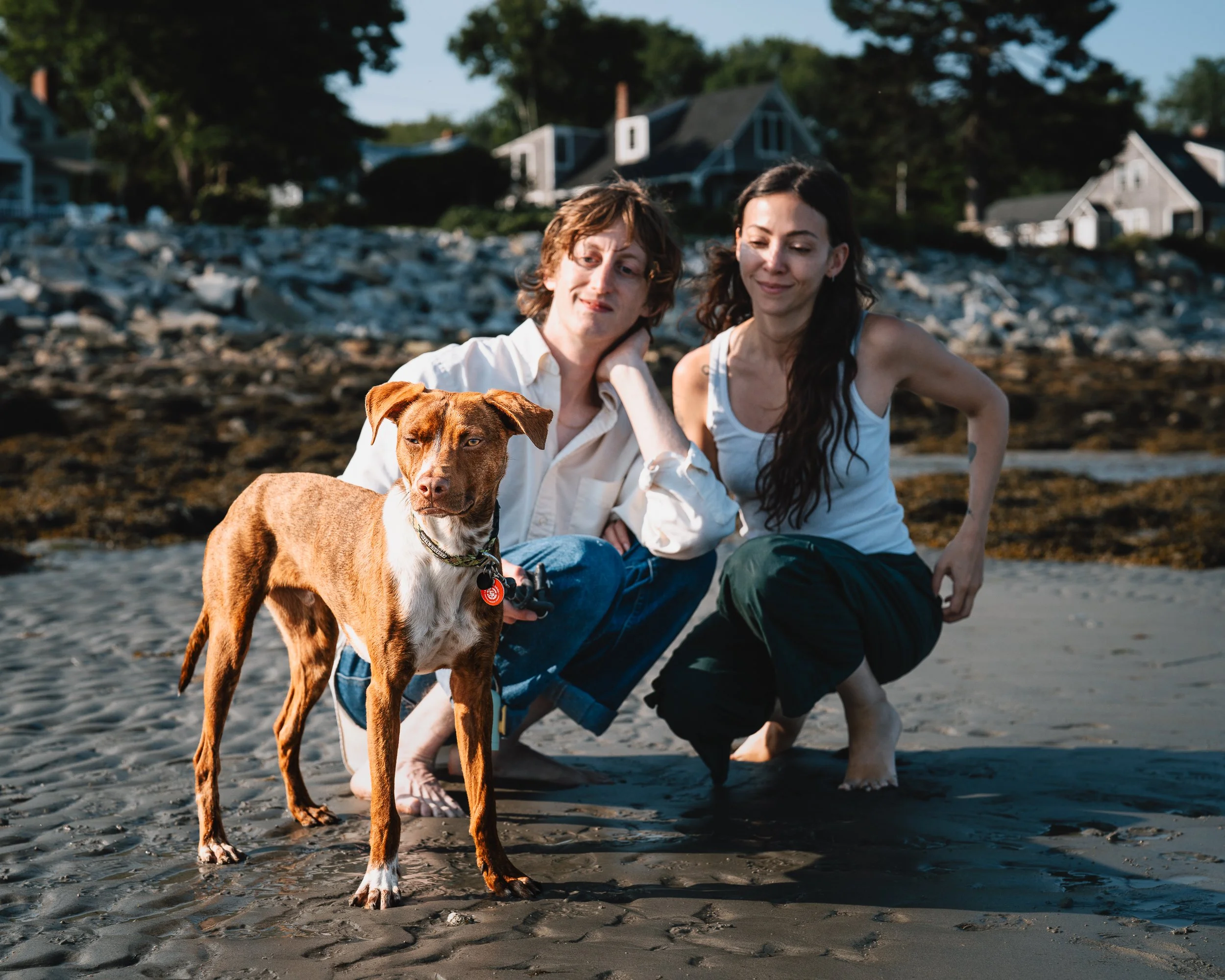 Emilie and Greg crouching beside Beso on the beach
