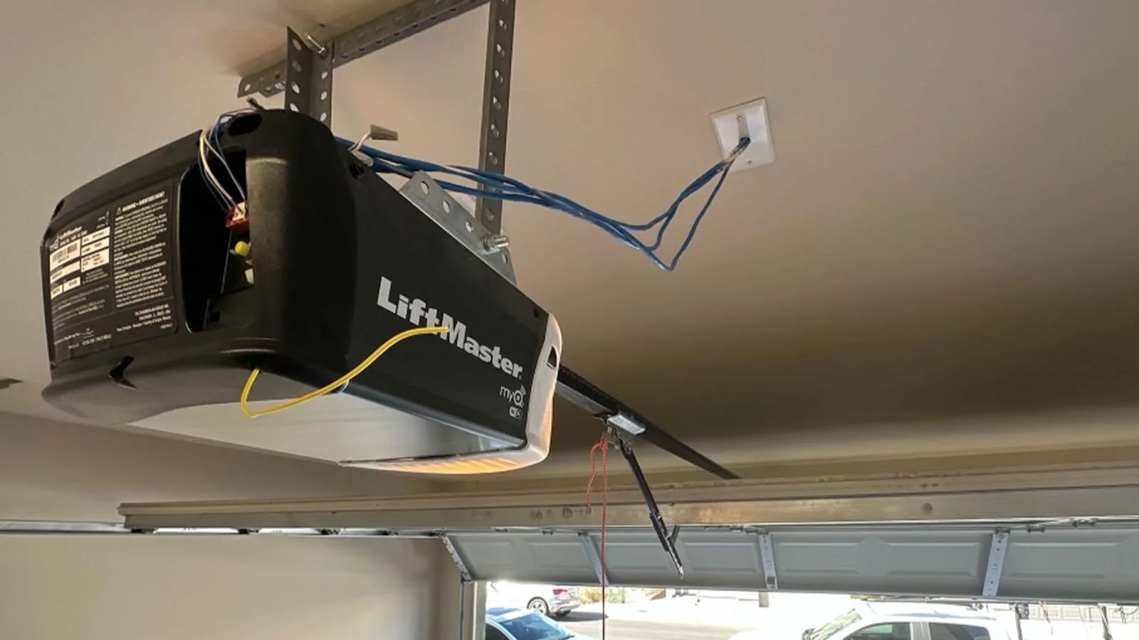 Garage door opener with exposed wiring and partially open garage door.
