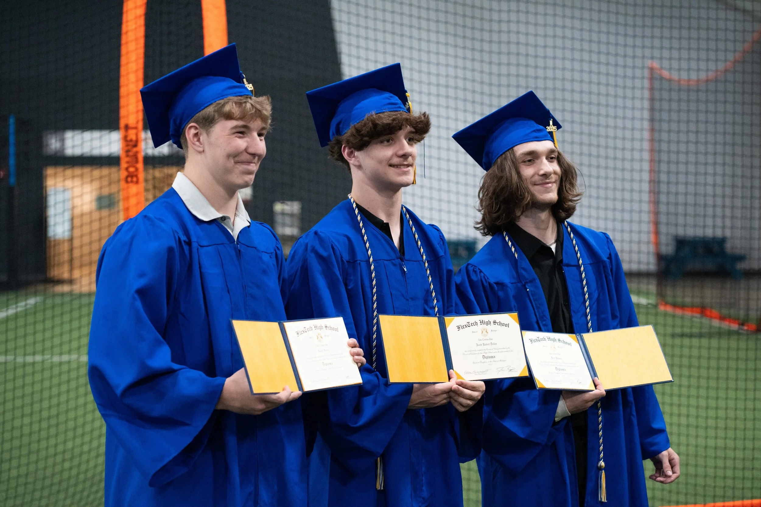 FlexTech Brighton graduates in blue caps and gowns celebrating their high school achievements on the field, representing alternative and accelerated learning success.