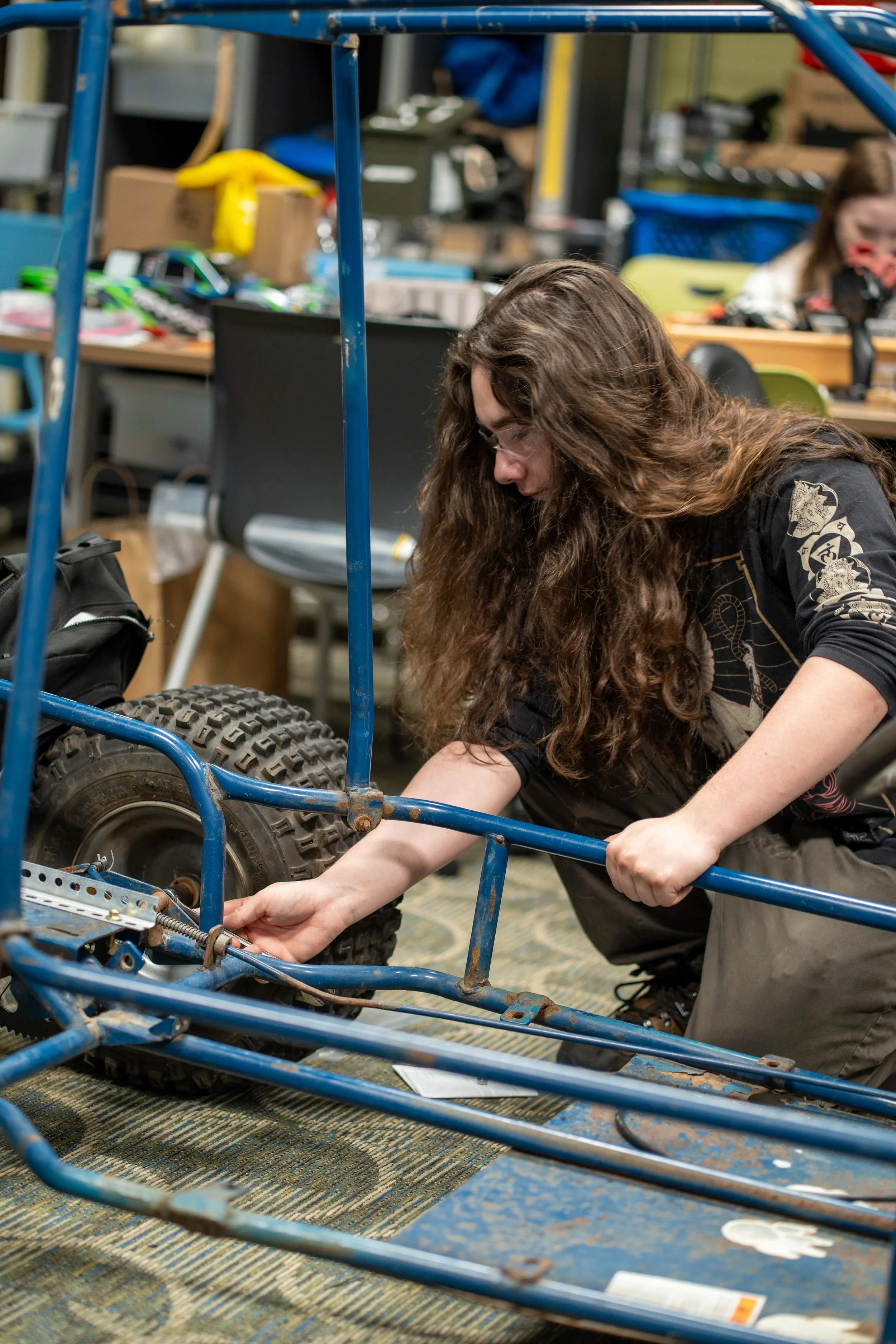 A young woman with long curly hair working on the frame of a small go-kart in a workshop at FlexTech Brighton.