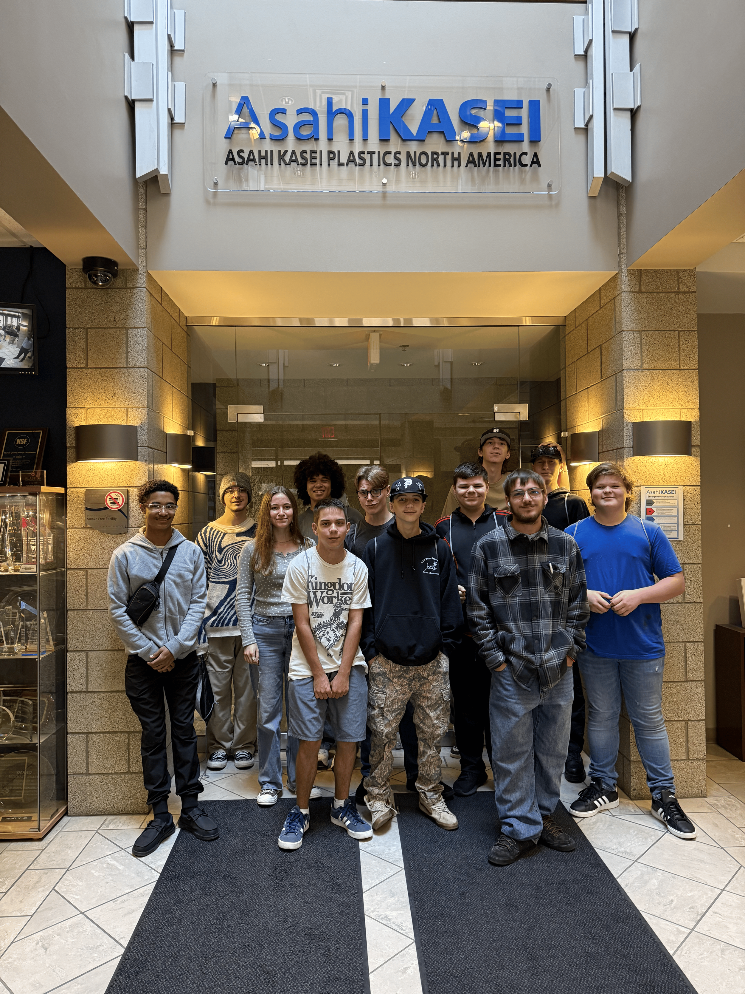 FlexTech Brighton high school students standing in front of Asahi KASEI Plastics North America entrance at a corporate building.