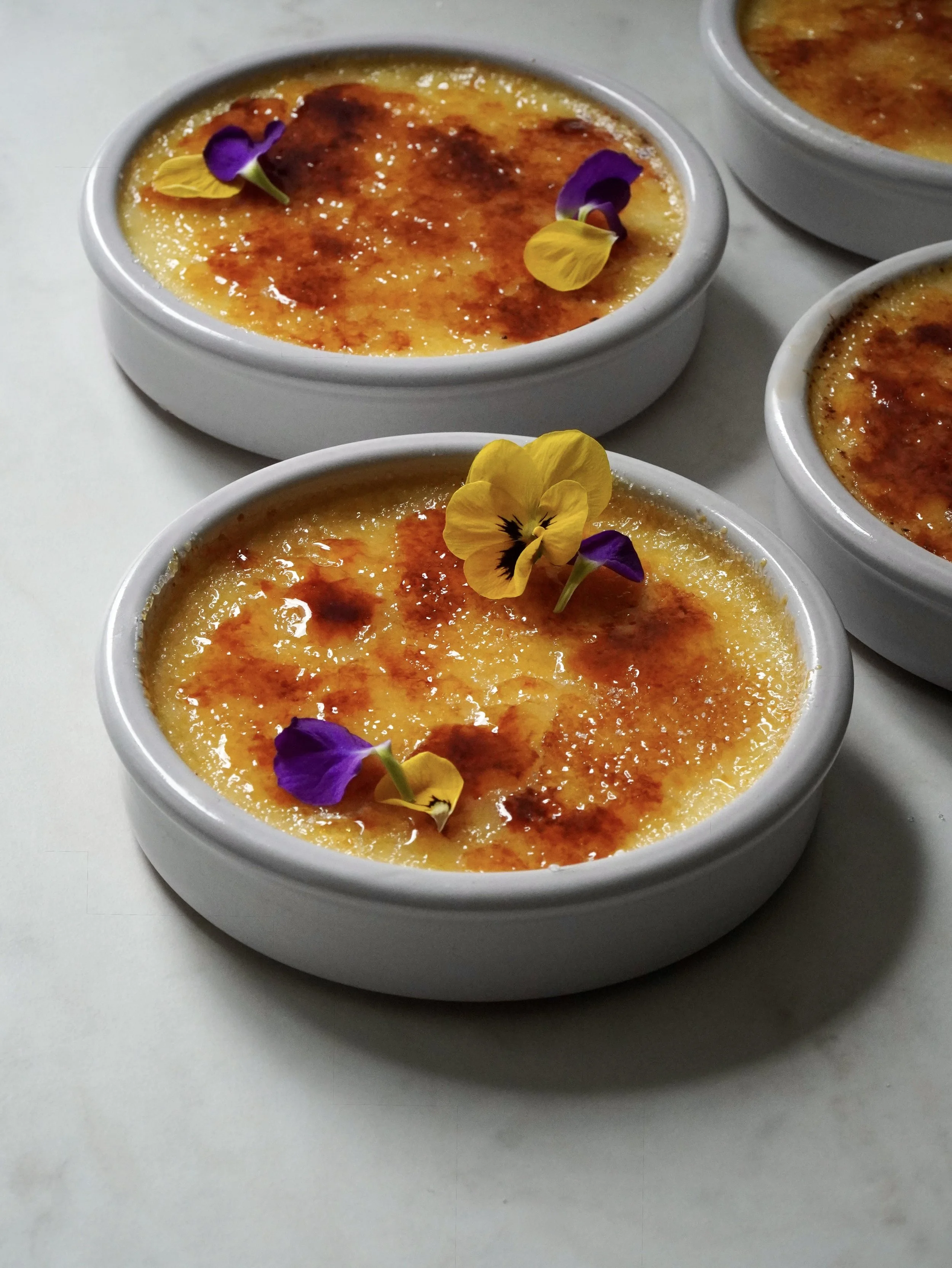 Two ramekins of crème brûlée with caramelized sugar topping, one with a spoon