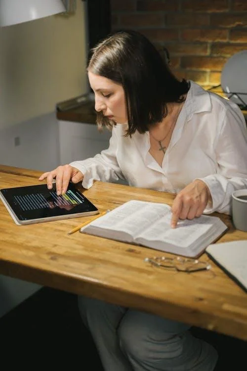 Hands holding a Bible next to a tablet, representing balanced technology use and Christian spiritual growth
