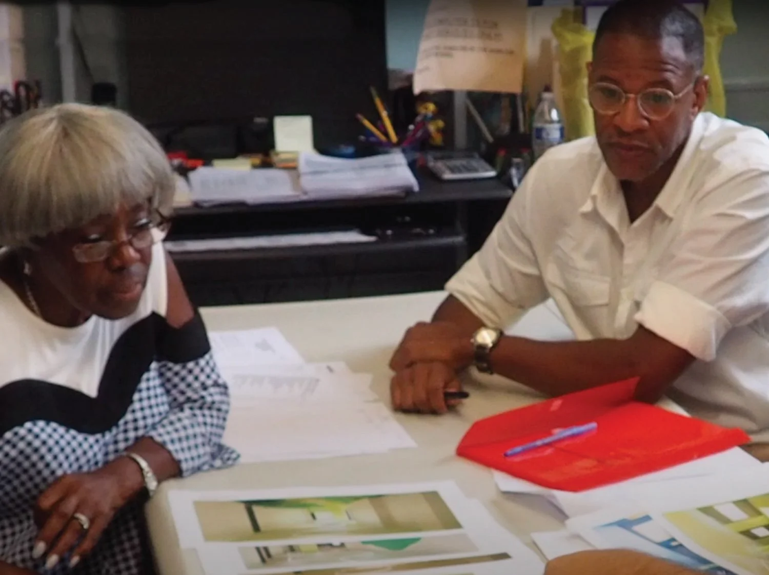  Two people working together at a table, looking at printed materials, indicating collaboration in a community setting. 