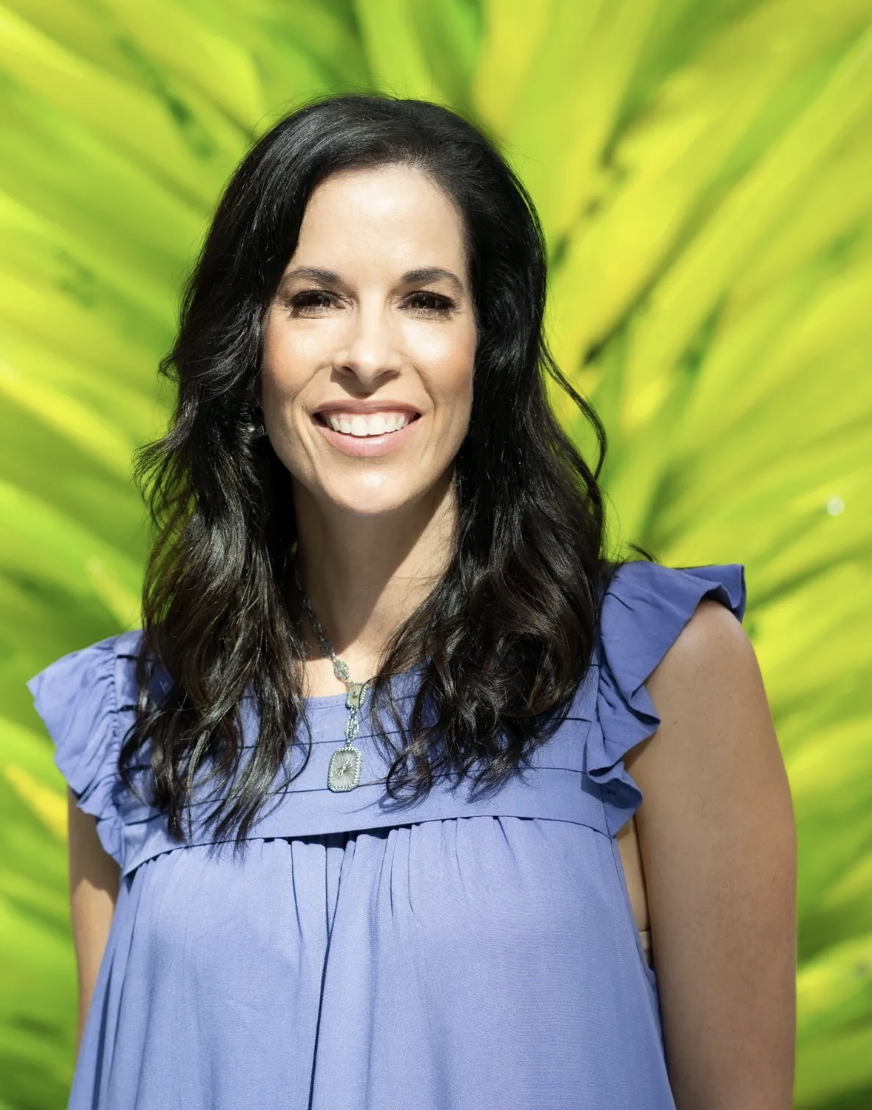 Smiling woman with dark hair in purple dress, standing in front of a vibrant green background.