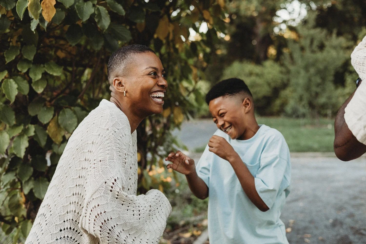 A woman and a young girl are laughing and having fun outdoors, with trees in the background during an outdoor family photo session at the Botanical Garden, Montreal