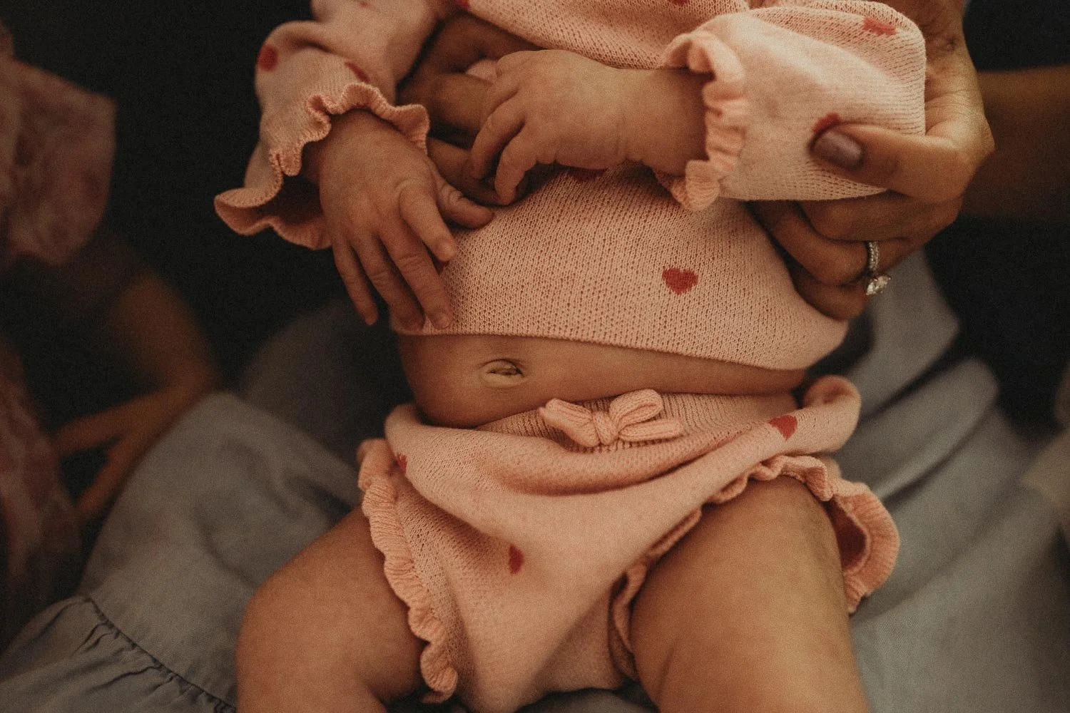 A closed-up photo of a newborn belly picking ender her blouse and little hands while being help by her mom, captured during an in-home Montreal newborn photoshoot.