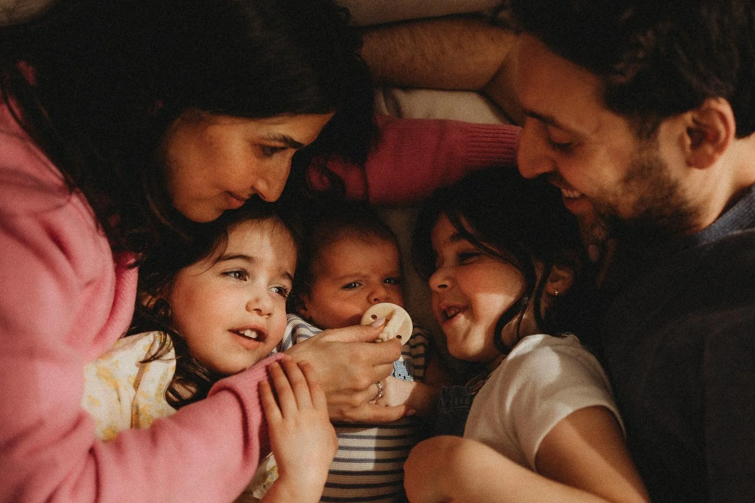 Family of five cuddling on a couch, smiling and hugging captured during an in-home family photoshoot in Hampstead, Montreal