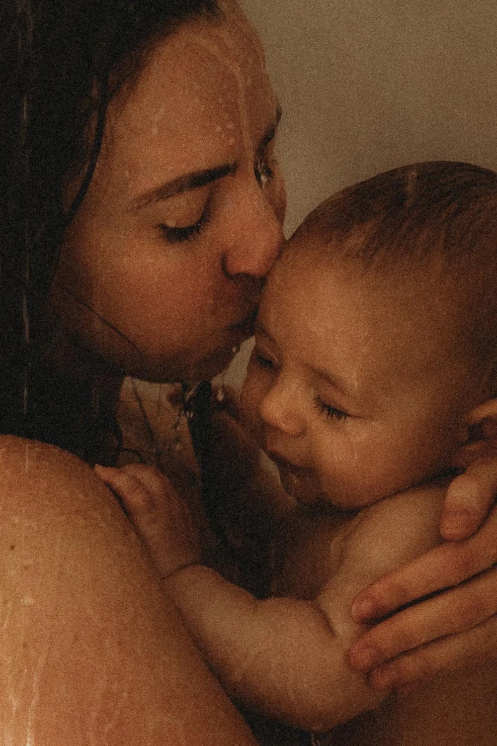 A woman and a young child sharing an intimate moment, with the woman kissing the child's forehead and the child smiling gently during an in-home shower motherhood photo session at Dorval Montreal