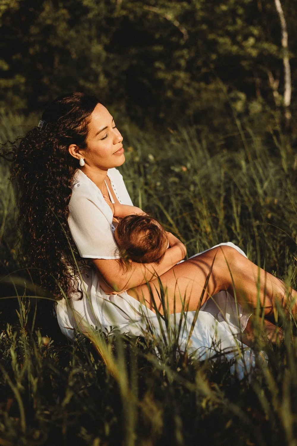 A photo of a mother breastfeeding her baby with her eyes closed captured during an outdoor motherhood photoshoot at Cap-Saint-Jacques, Montreal 