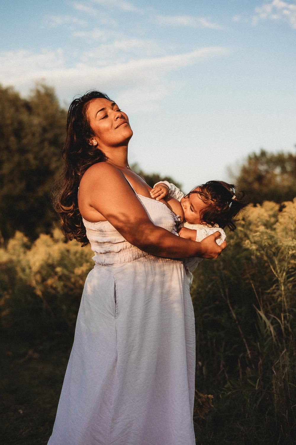 Mom breastfeeding her baby with closed eyes in a tender moment captured during an outdoor motherhood photoshoot at Boucherville Island, Montreal