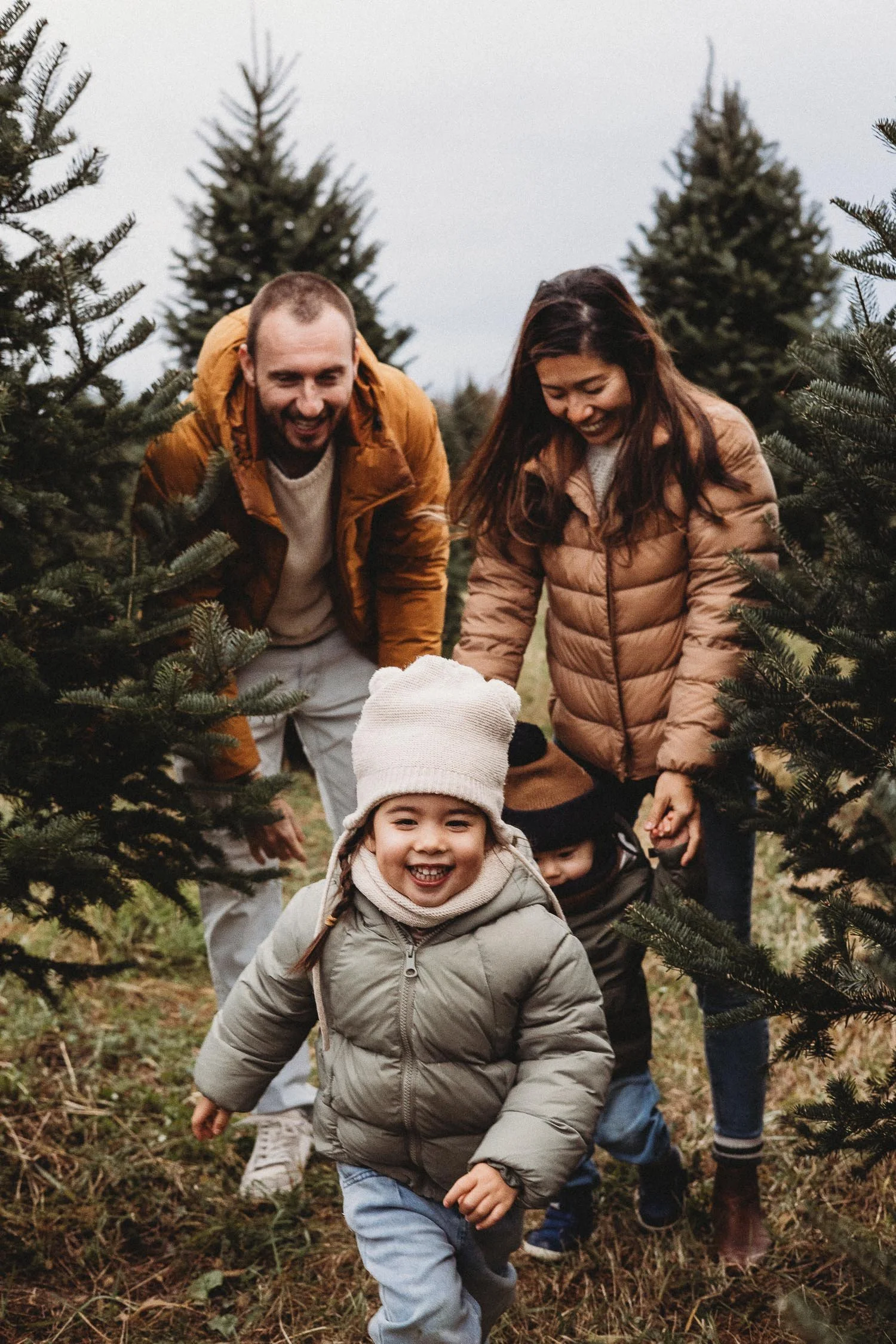 Kids running towards the camera while parents are smiling during an outdoor  Montreal family photoshoot