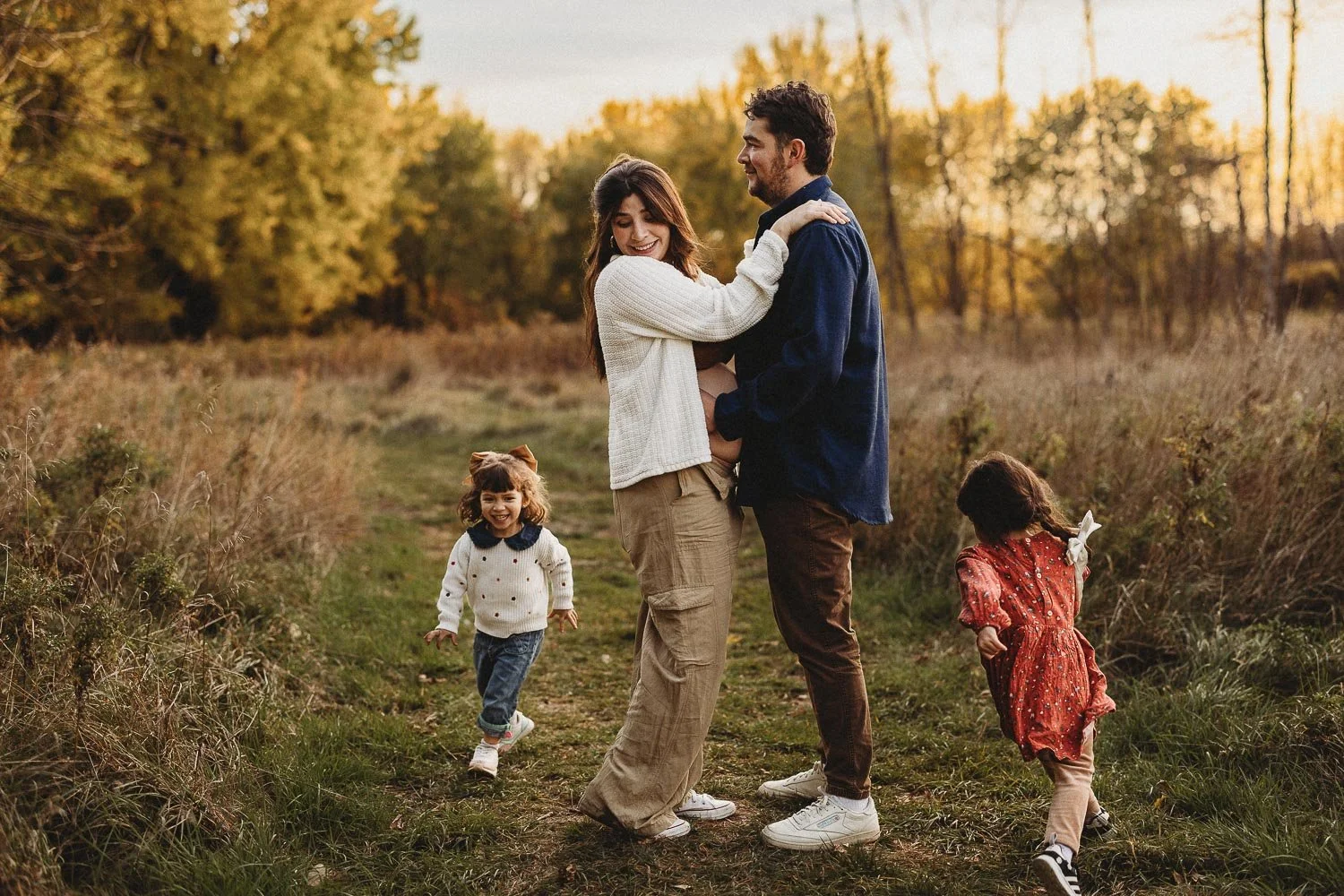 Kids running around parents while the parents are smiling and looking at the kids, captured during an outdoor family photoshoot in Boucherville Island