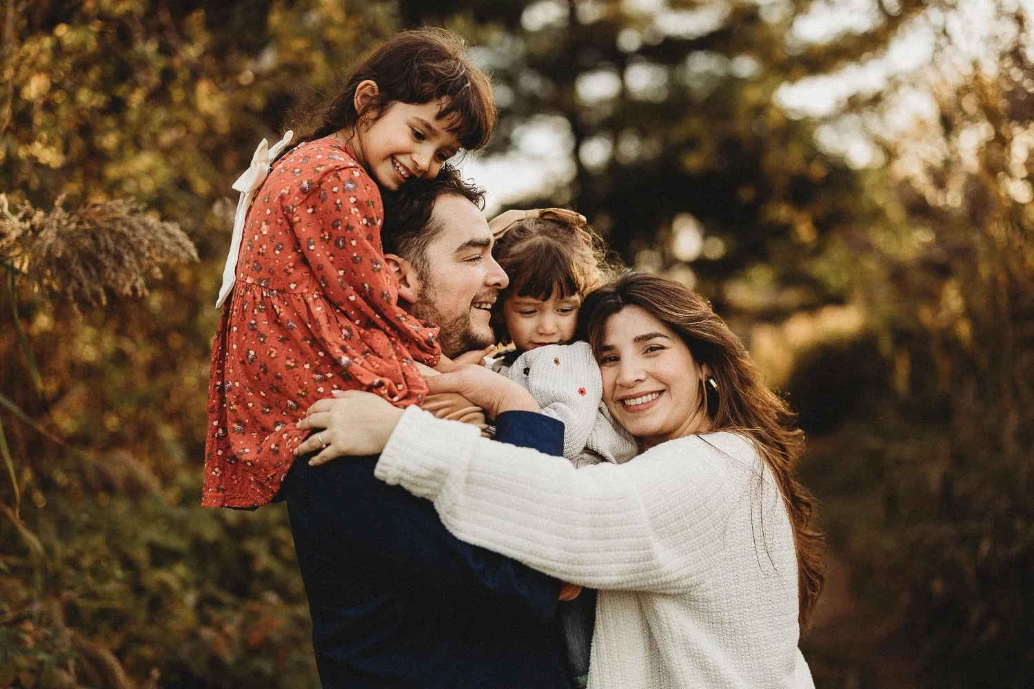 Family of four hugging tenderly while mom is looking at the camera, captured during an outdoor family photo session in Boucherville Island