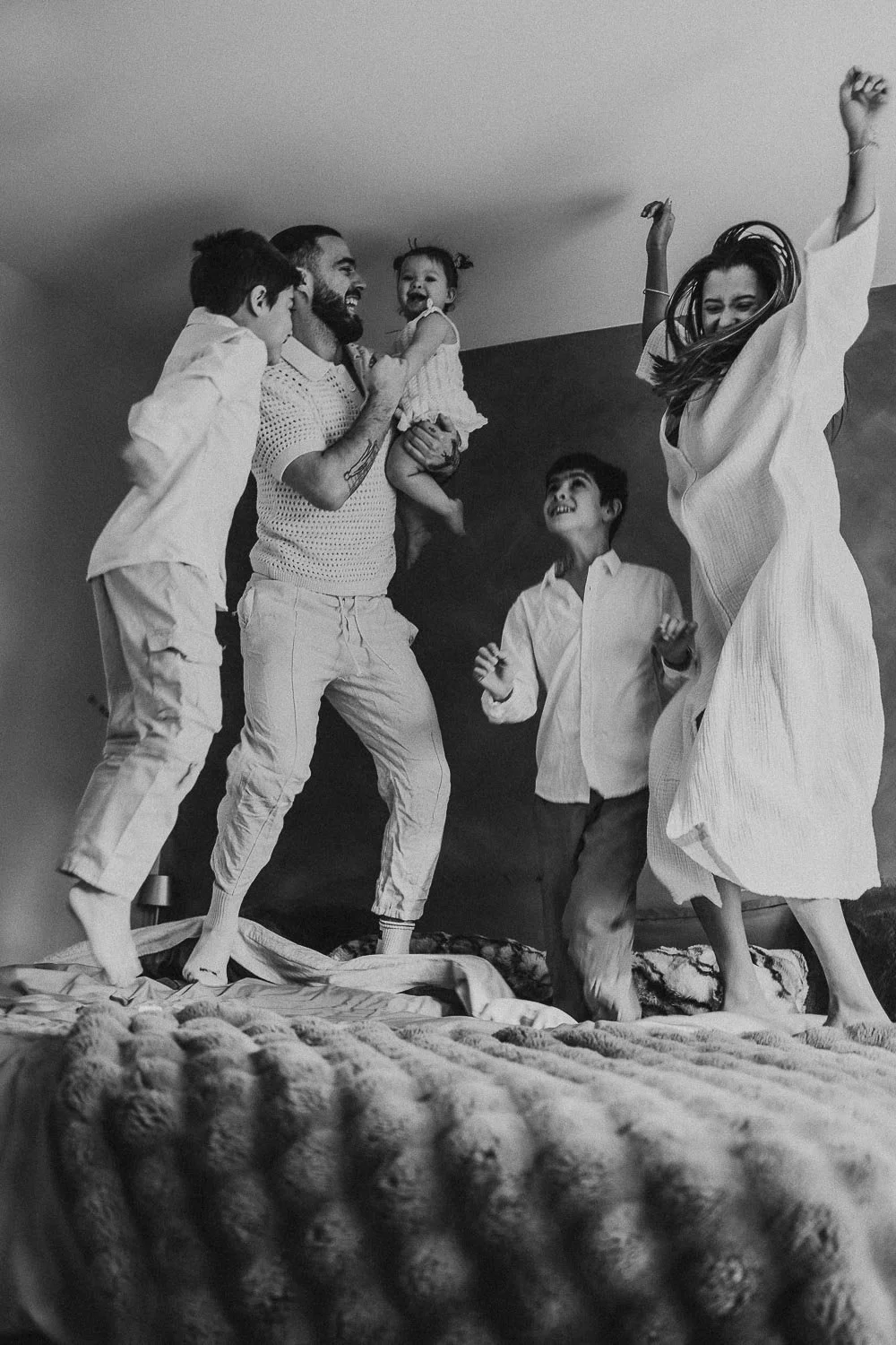 Family jumping on bed while laughing during a candid in-home family photoshoot in montreal
