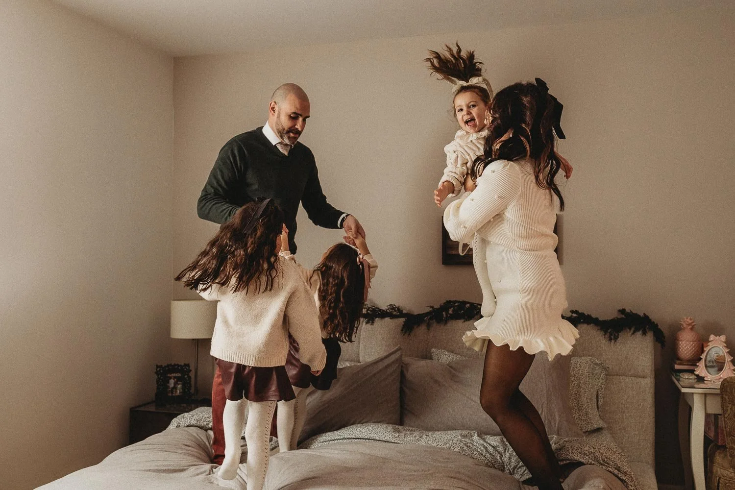 Family of five laughing and jumping on a bed, captured during an in-home family photo session in Montreal