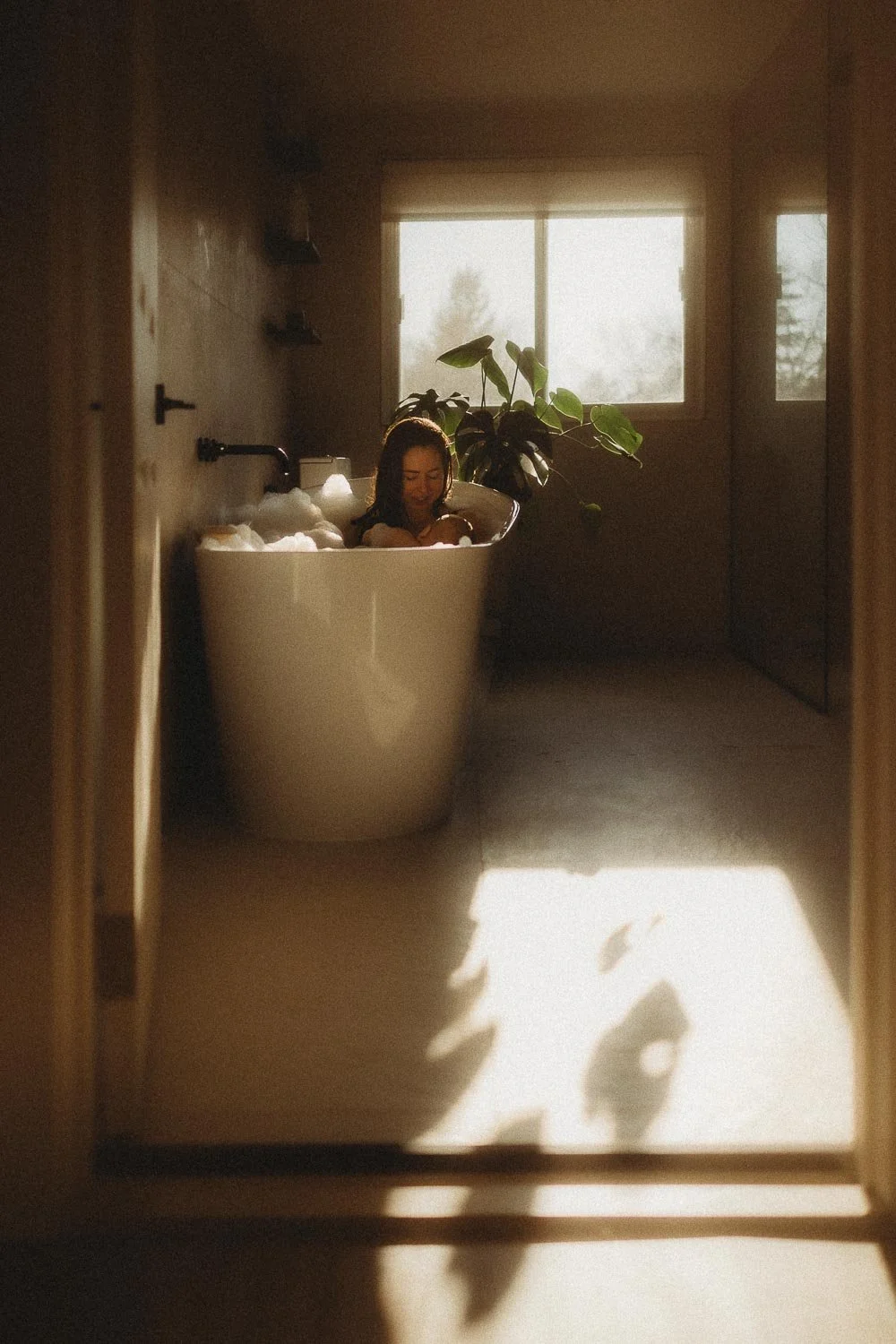 Photo of a mom breastfeeding her baby in a bathtub during golden hour with the sunlight shinning through the window, captured during an in-home Motherhood photoshoot in Dorval, Quebec