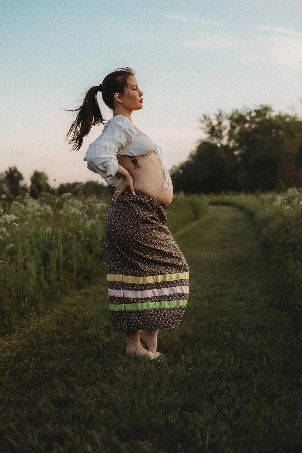 A Mohawk pregnant woman posing and looking at horizon wearing a traditional skirt surrounded by natured and captured during an outdoor maternity photoshoot in Boucherville Island, Quebec