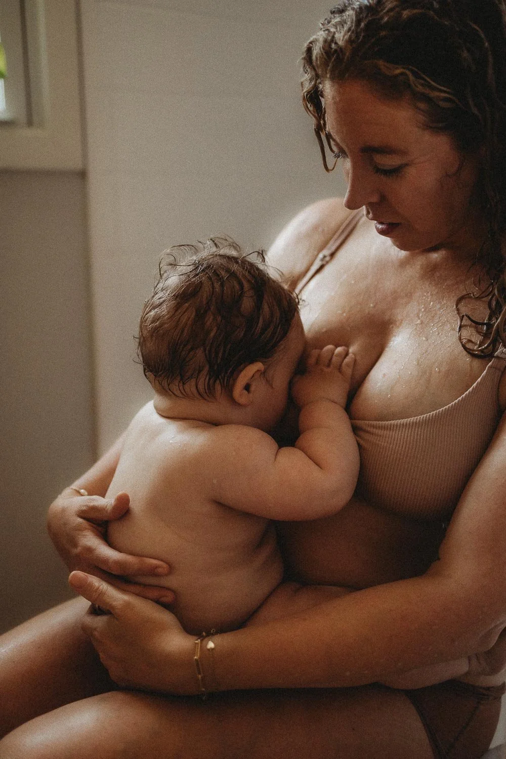 A Montreal Motherhood photoshoot of a mom breastfeeding her baby boy while droplets of water run through her body, she holds her baby closely while looking at him 