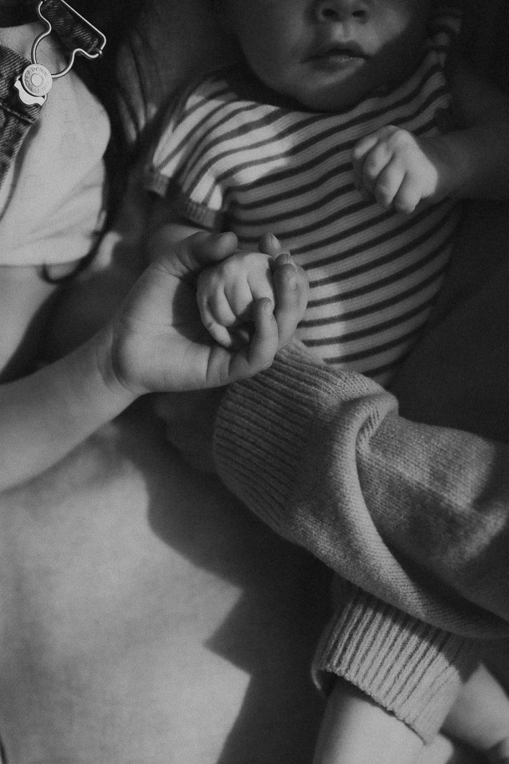 Close-up of an adult holding a child's hand, both with clenched fists, in a black and white photo captured during an in-home newborn photoshoot in Hampstead, Montreal
