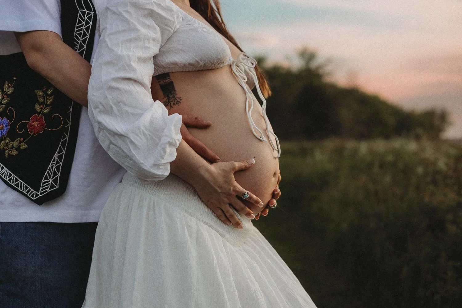 A closed up photo of a pregnant woman being held by her partner who is behind her during a golden hour photoshoot in Boucherville Island, Quebec