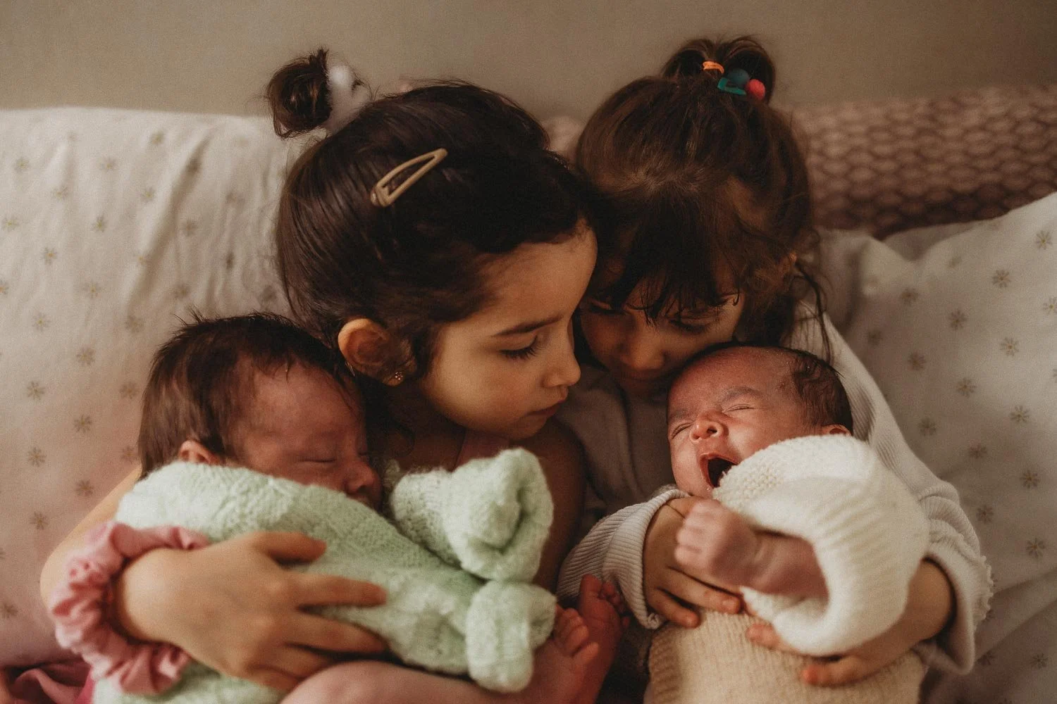 Two sisters holding and cuddling their twin sibling babies at an in-home newborn photo session in La Salle, Montreal
