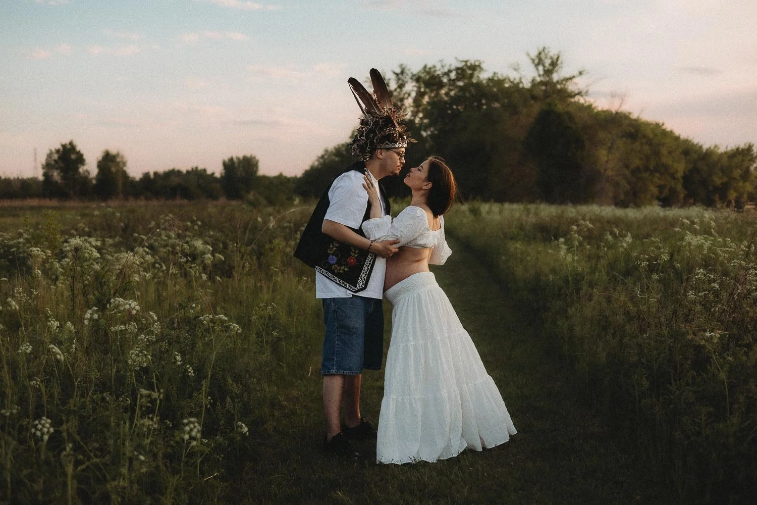 A Mohawk pregnant woman and her partner leaning towards each other in the middle of nature, captured during an outdoor maternity photoshoot in Boucherville Island, Quebec