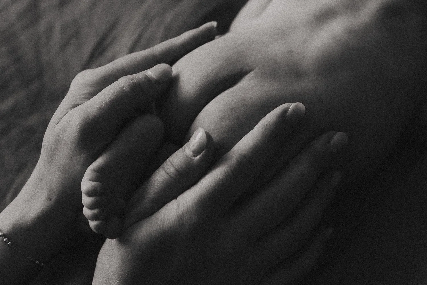 A close-up b&w photo of a newborn baby's bump gently covered by her mother's hands, we also see one of the baby's foot during an in-home newborn photo session that happened in The West Island, Montreal