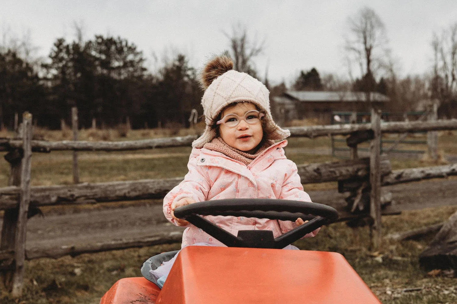 A photo of a toddler girl riding a tractor at Quinn Farm during an outdoor fall photoshoot in Notre-Dame-de-l'Île-Perrot