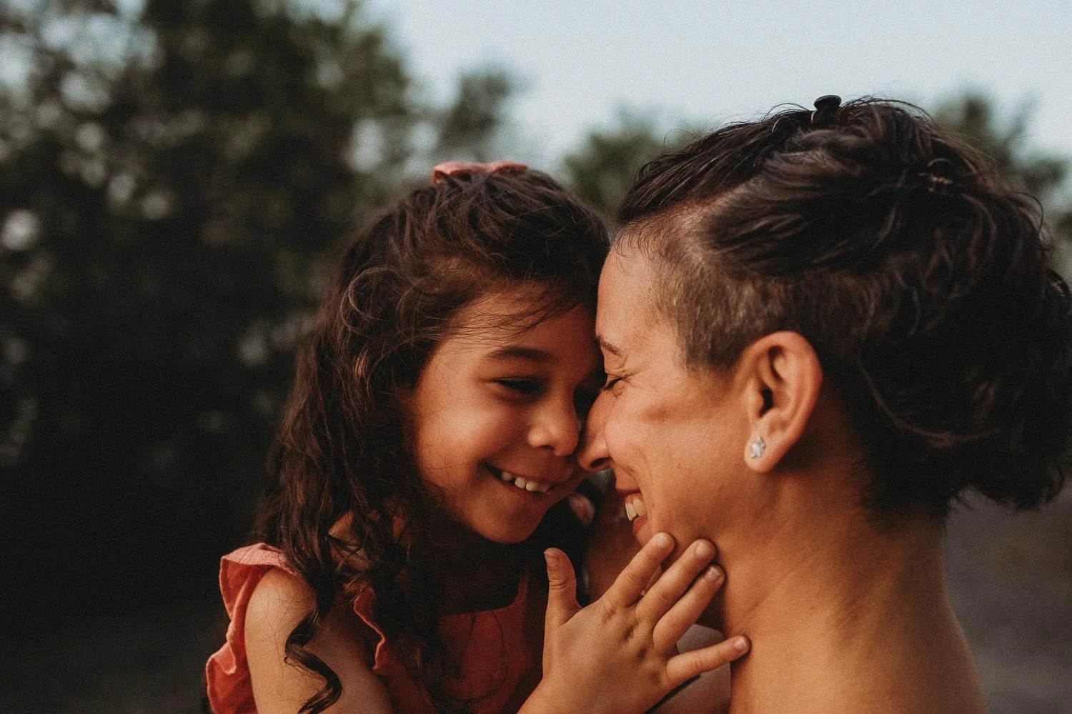 Mother and her young daughter nose to nose, both laughing, during a summer family session near Montreal