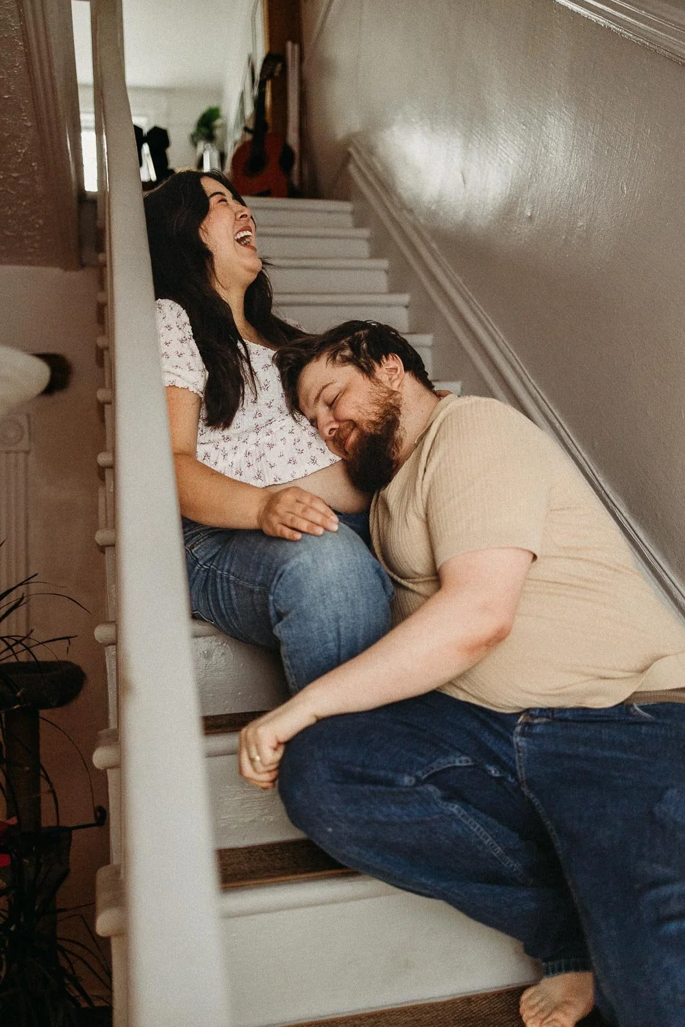 A joyful pregnant woman and a man sharing a moment of happiness on a staircase, laughing and relaxed. during a maternity photo session in West Montreal